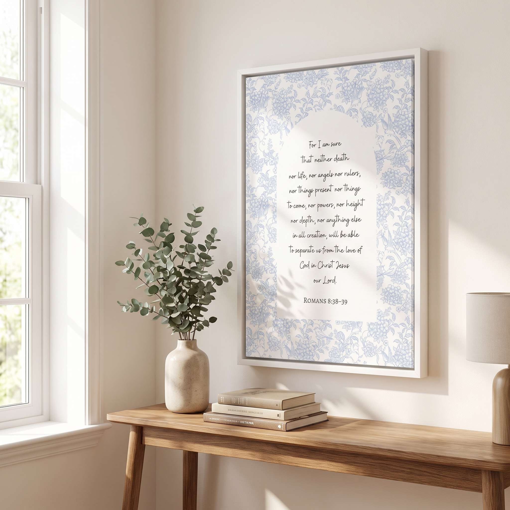 Framed Christian floral scripture wall art titled Romans 8:38–39 featuring "Nothing can separate us from the love of God" with blue botanical artwork, displayed in a white frame on a light wall above a wooden console table in a bright bedroom near a window.