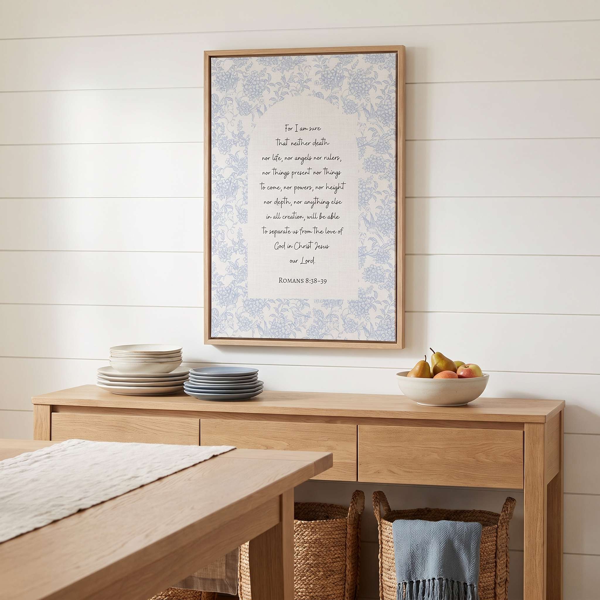 Framed Christian floral wall art titled Romans 8:38–39 featuring "Nothing can separate us from the love of God" with blue botanical artwork, displayed in a light wood frame on a shiplap wall above a wooden sideboard in a bright dining room.