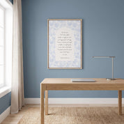 Framed Christian floral scripture wall art titled Romans 8:38–39 featuring "Nothing can separate us from the love of God" with blue botanical artwork, displayed in a light wood frame on a slate blue wall above a modern wooden desk in a bright coastal workspace.