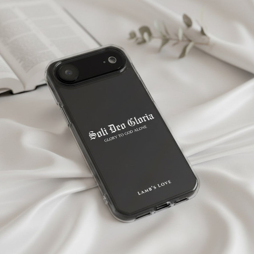 Christian MagSafe iPhone case with Soli Deo Gloria “Glory to God Alone” design on a black phone case displayed on white silk fabric with an open Bible