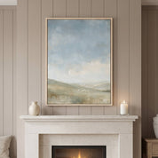 Framed The Earth Is the Lord’s Christian landscape with rolling hills and sheep above a white fireplace mantel with a vase and candle on a paneled wall.