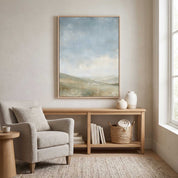 The Earth Is the Lord’s Christian landscape wall art above a wooden console with pottery, books and a woven basket beside a gray armchair.
