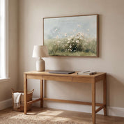 Framed vintage Psalm 103:8 wildflower landscape canvas wall art hanging above a light wood desk with a lamp and laptop in a warm modern workspace.
