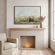 Framed vintage Psalm 103:8 wildflower landscape canvas wall art hanging above a modern cream fireplace mantel with a ceramic vase and armchair in a soft organic modern living room.