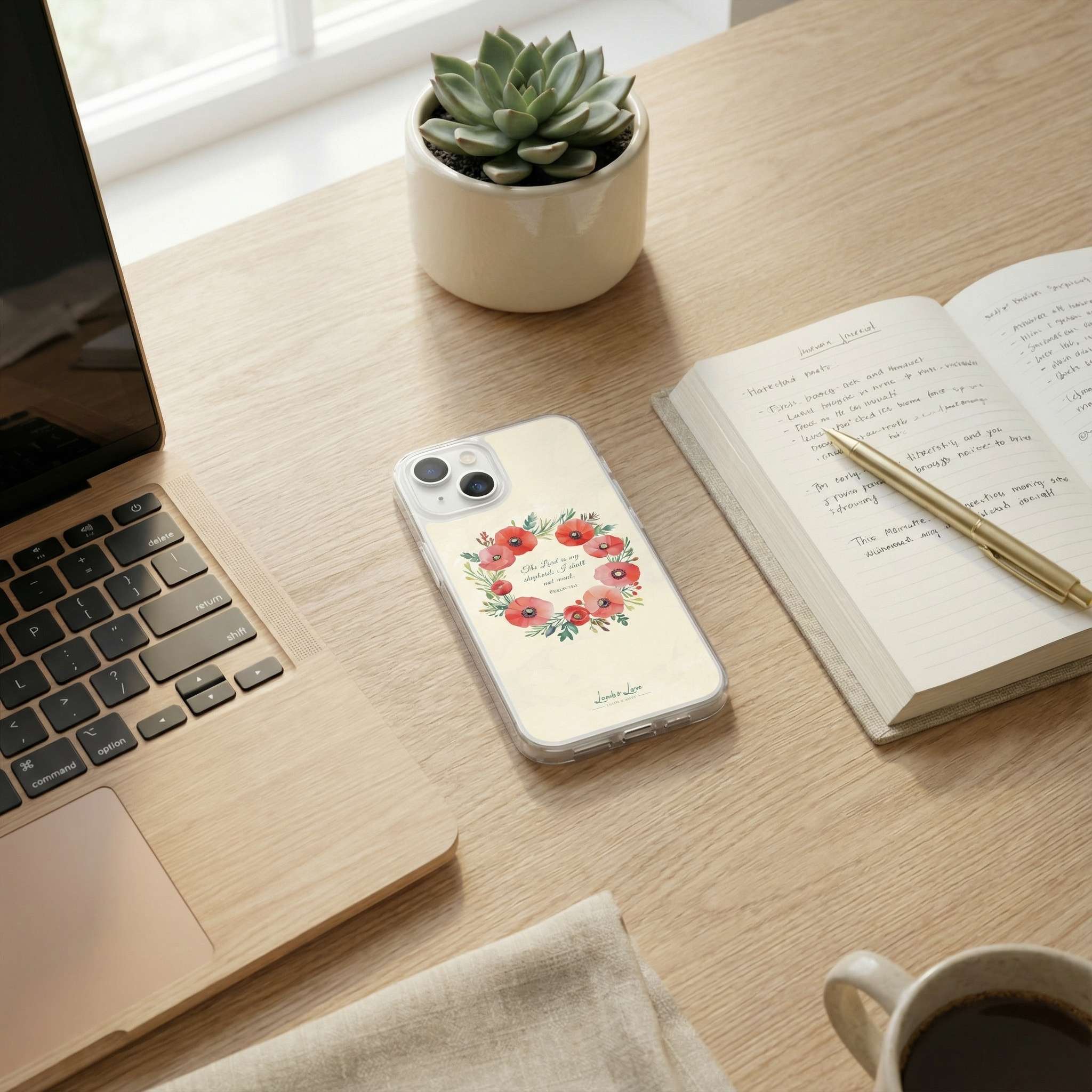 Laptop, phone with floral case, notebook, pen, and succulent on a wooden desk.