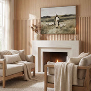 A framed vintage Christian art print depicting Jesus walking with a flock of sheep hangs on a wood-paneled wall above a white fireplace mantel with two beige armchairs in a cozy, organic modern living room.