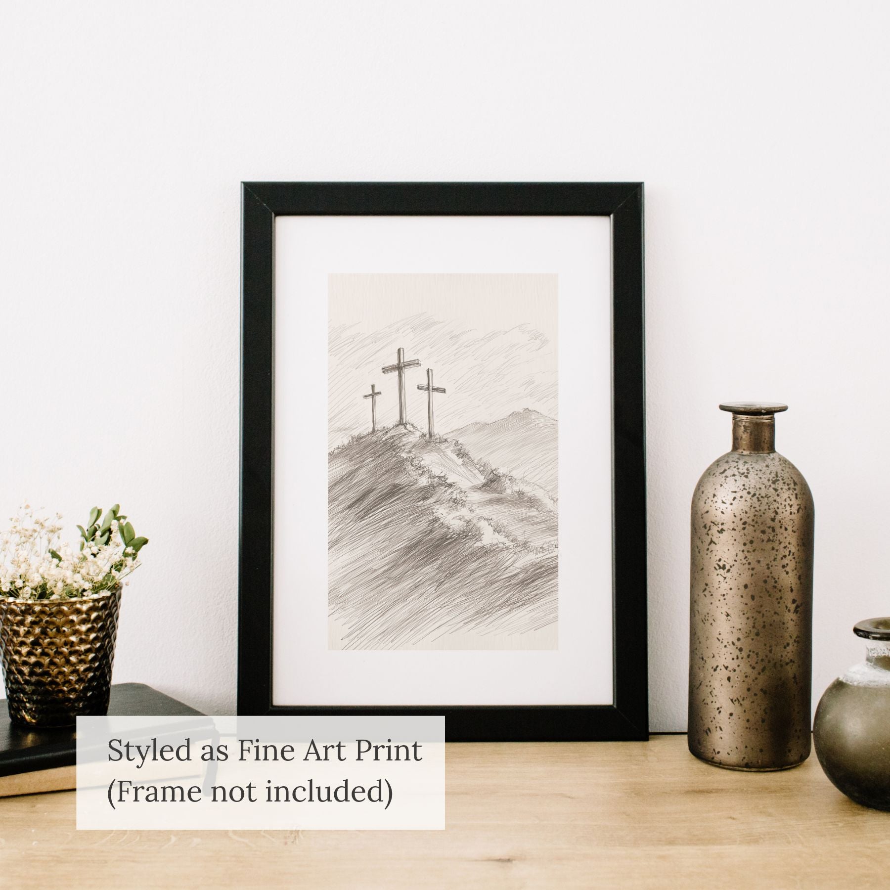 Minimalist Three Crosses fine art print in a black frame, styled on a wooden tabletop next to rustic ceramic vases.