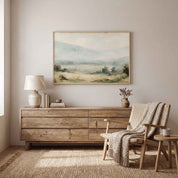 Framed vintage Proverbs 3:5-6 Christian landscape canvas wall art featuring a misty valley scene hanging on a light beige wall above a rustic wooden dresser with a ceramic lamp, stacked books, and a woven armchair in a warm neutral bedroom.