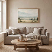 Framed vintage Proverbs 3:5-6 Christian landscape canvas wall art featuring a misty valley scene hanging on a light beige wall above a warm beige sofa and rustic wooden coffee table in a modern organic living room.