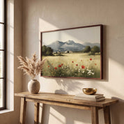 A framed landscape painting of a mountain valley with red poppies hangs on a beige wall above a rustic wooden console table styled with a vase of dried grass and a gold bowl.