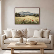 A framed landscape art print depicting a field of red poppies and white flowers with mountains in the background, hanging on a light beige wall above a modern white sofa with decorative pillows and a wooden coffee table.