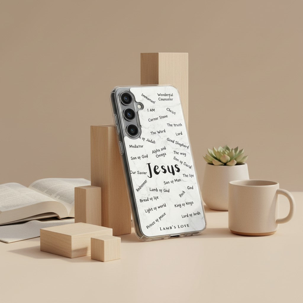 A Samsung Galaxy phone with a clear case featuring a typography design of the names of Jesus, including King of Kings and Prince of Peace, displayed on a wooden stand next to a white coffee mug and a small succulent.