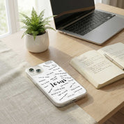 Phone with 'Jesus' case on a desk with laptop, notebook, and plant