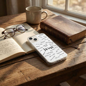 Phone with 'Jesus' case on a wooden table with books and a mug