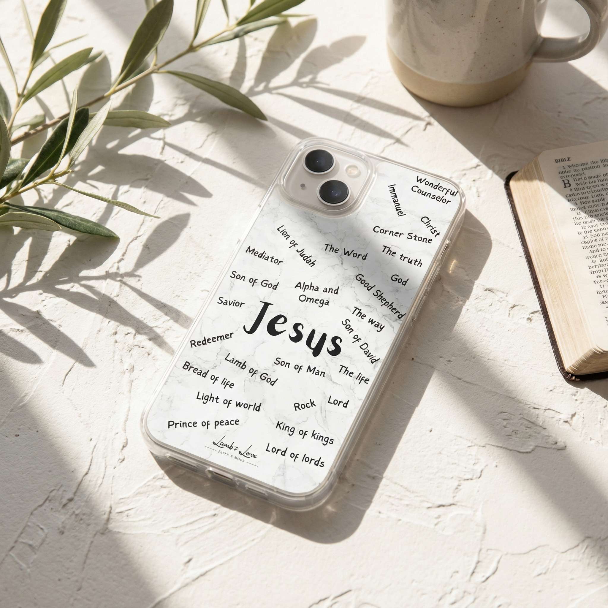 Phone case with 'Jesus' and religious text on a light surface with a plant and mug in the background